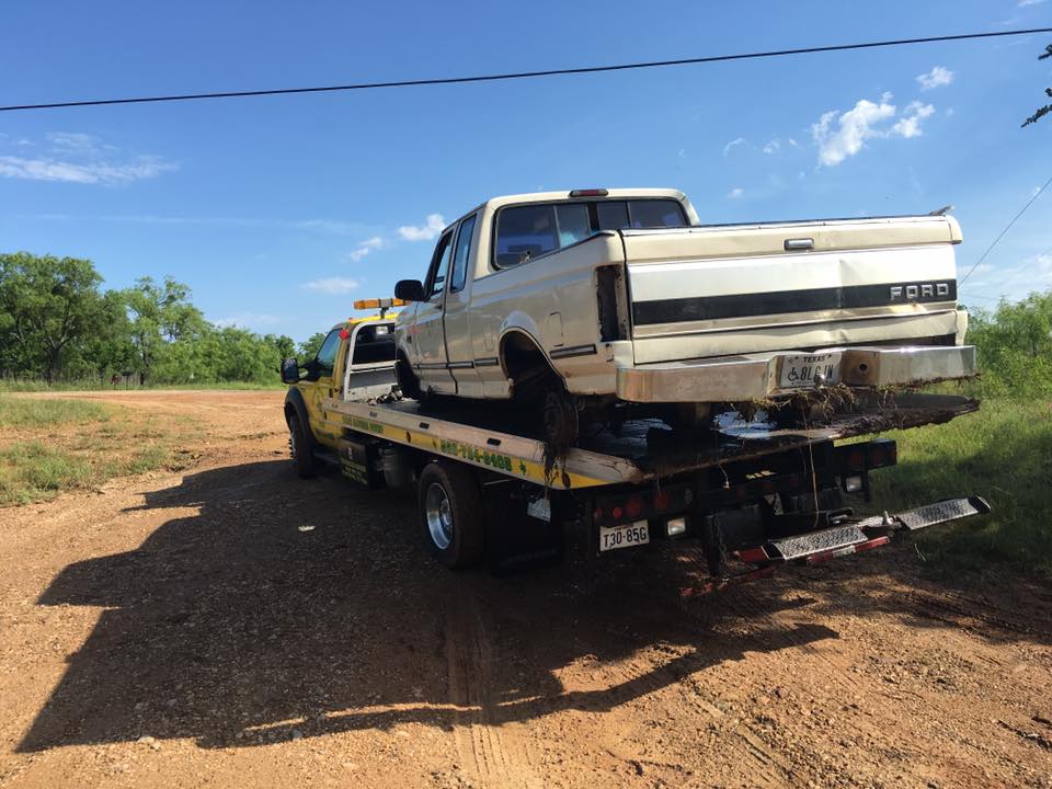 White Ford pickup truck secured on a flatbed tow truck on a dirt road